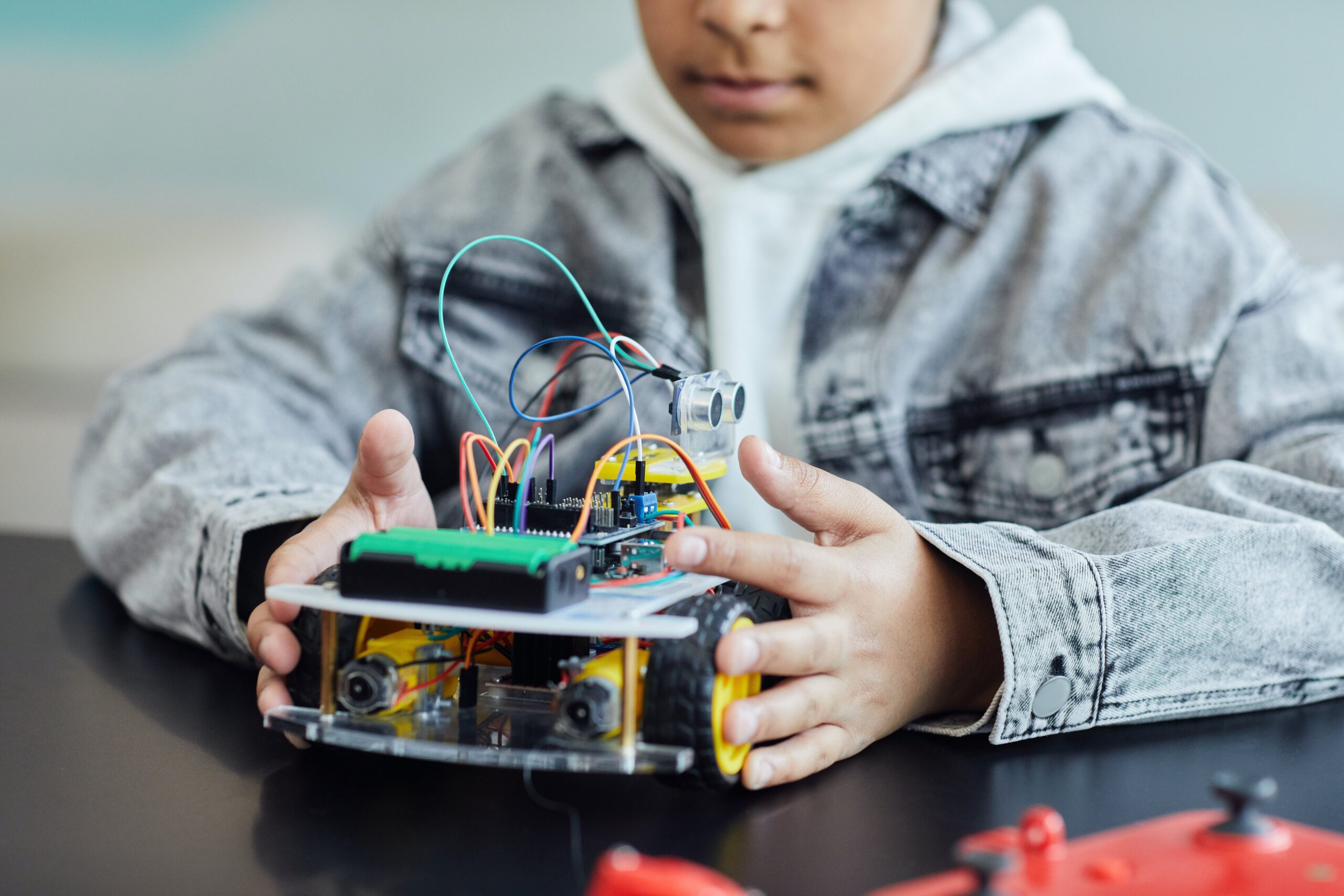 boy in denim jacket holding a toy with electric wires and a wheel  
