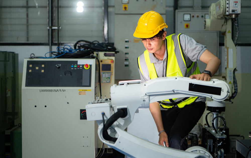 Technician who maintains a small robot arm the operation of a small robot arm used in industry is being repaired