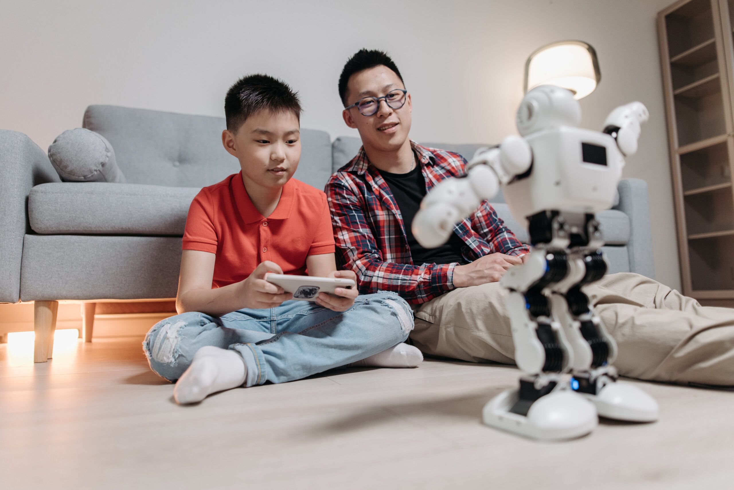 a man sitting next to a boy holding a remote controller playing with a robot toy
